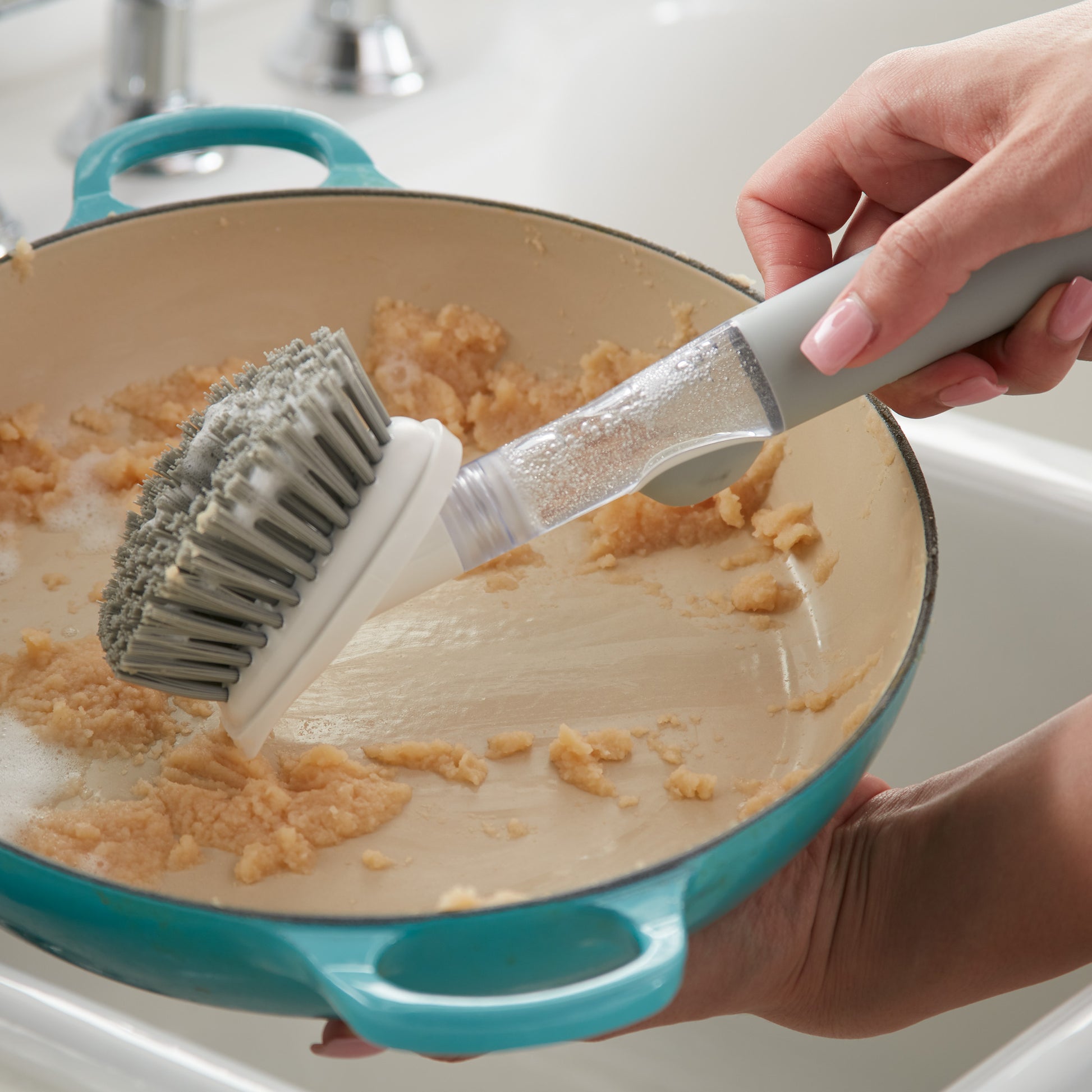 Norwex Soap-Dispensing Kitchen Scrub Brush in use - scrubbing stuck-on food in teal pan